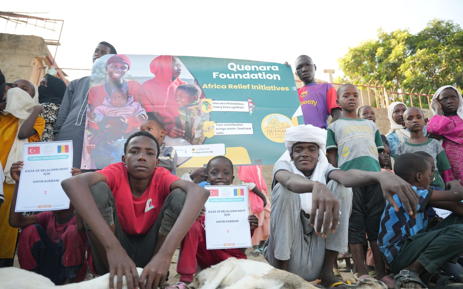 Young people in Chad holding Qurbani certificates beside the Quenara banner
