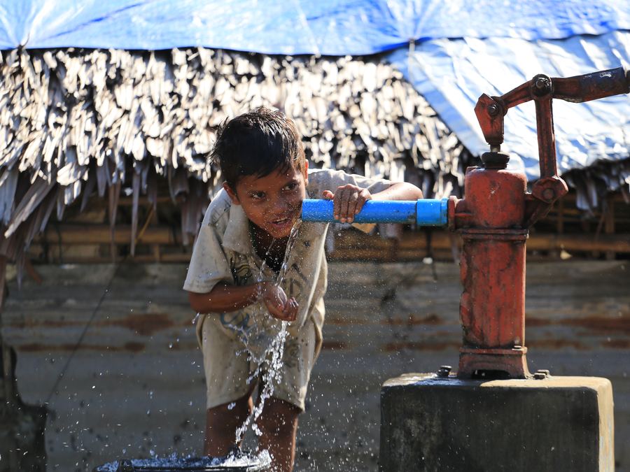 A child drinking water from a hand pump in a Rohingya camp