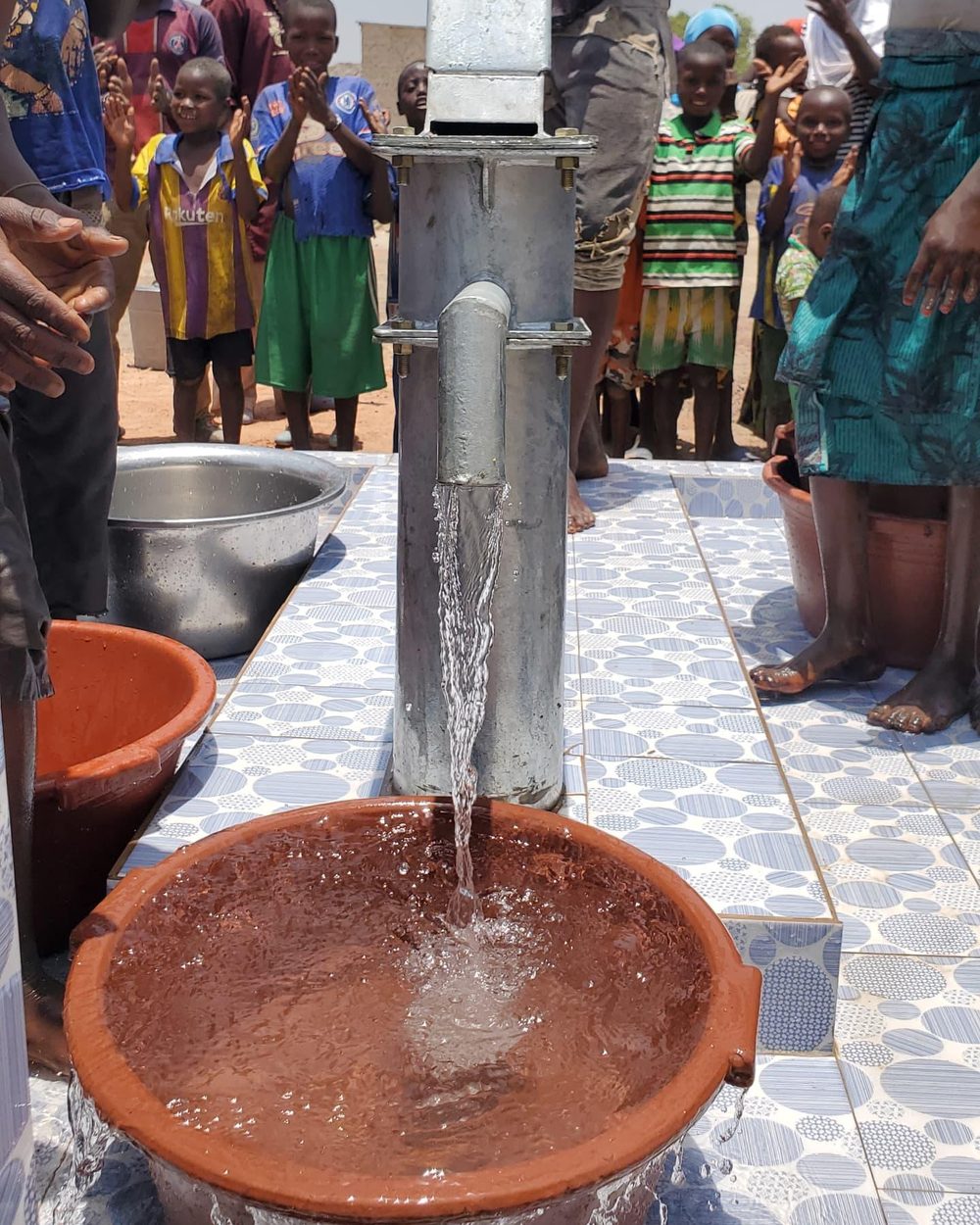 Clean water from a newly opened well and children waiting their turn